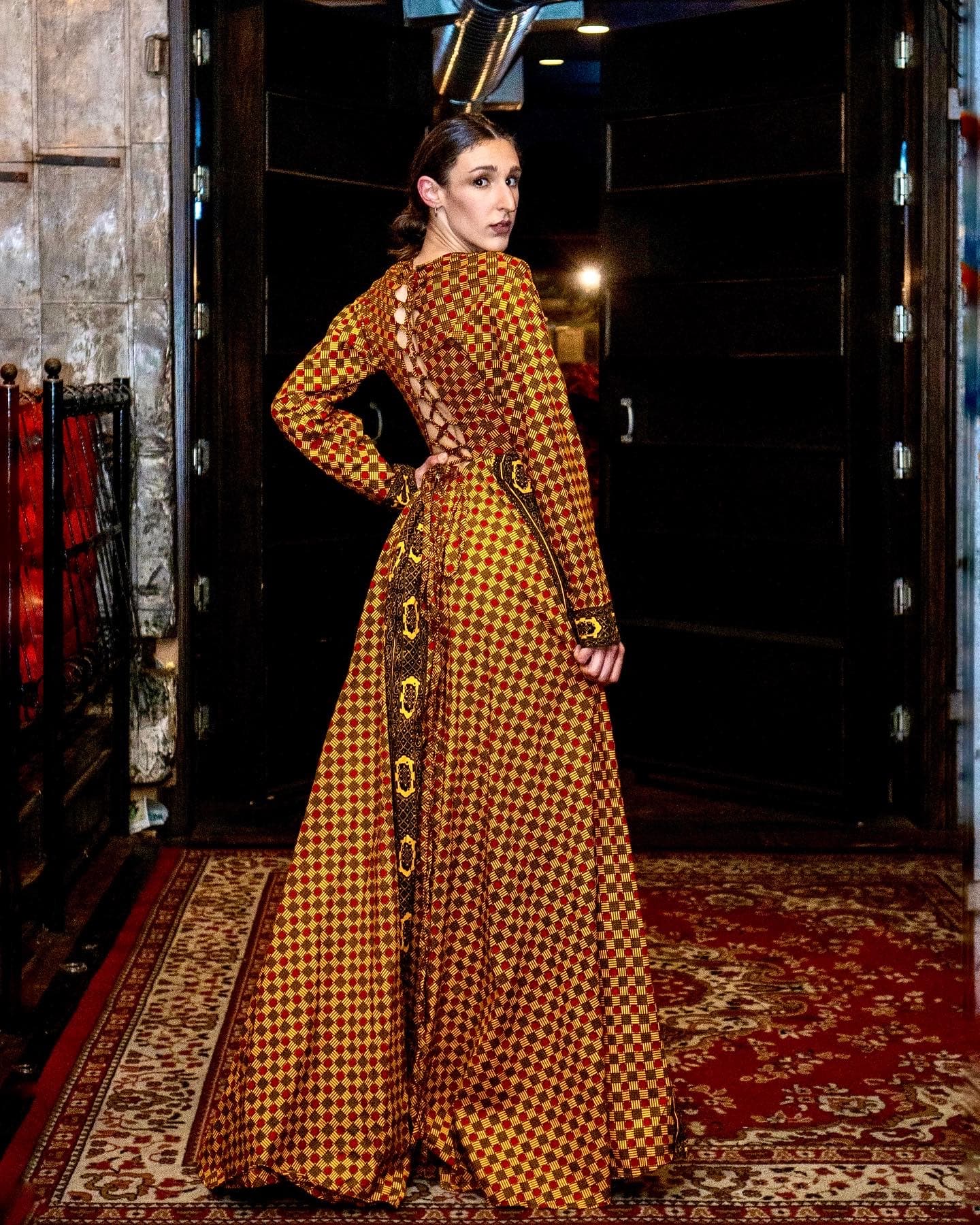 Fashion editorial, woman in gold houndstooth gown at venue entrance