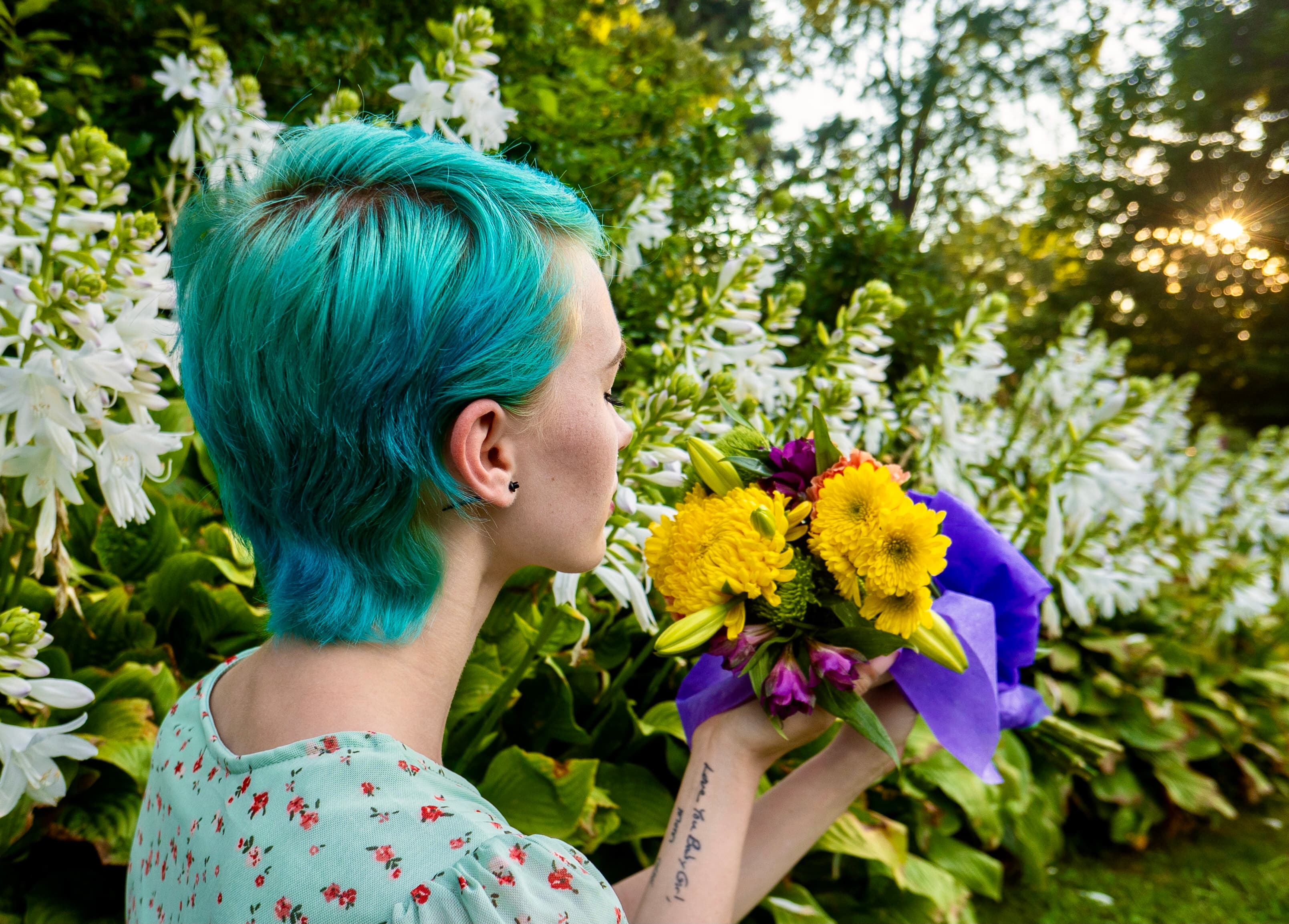 Lifestyle, woman with teal hair smelling wildflowers, back view
