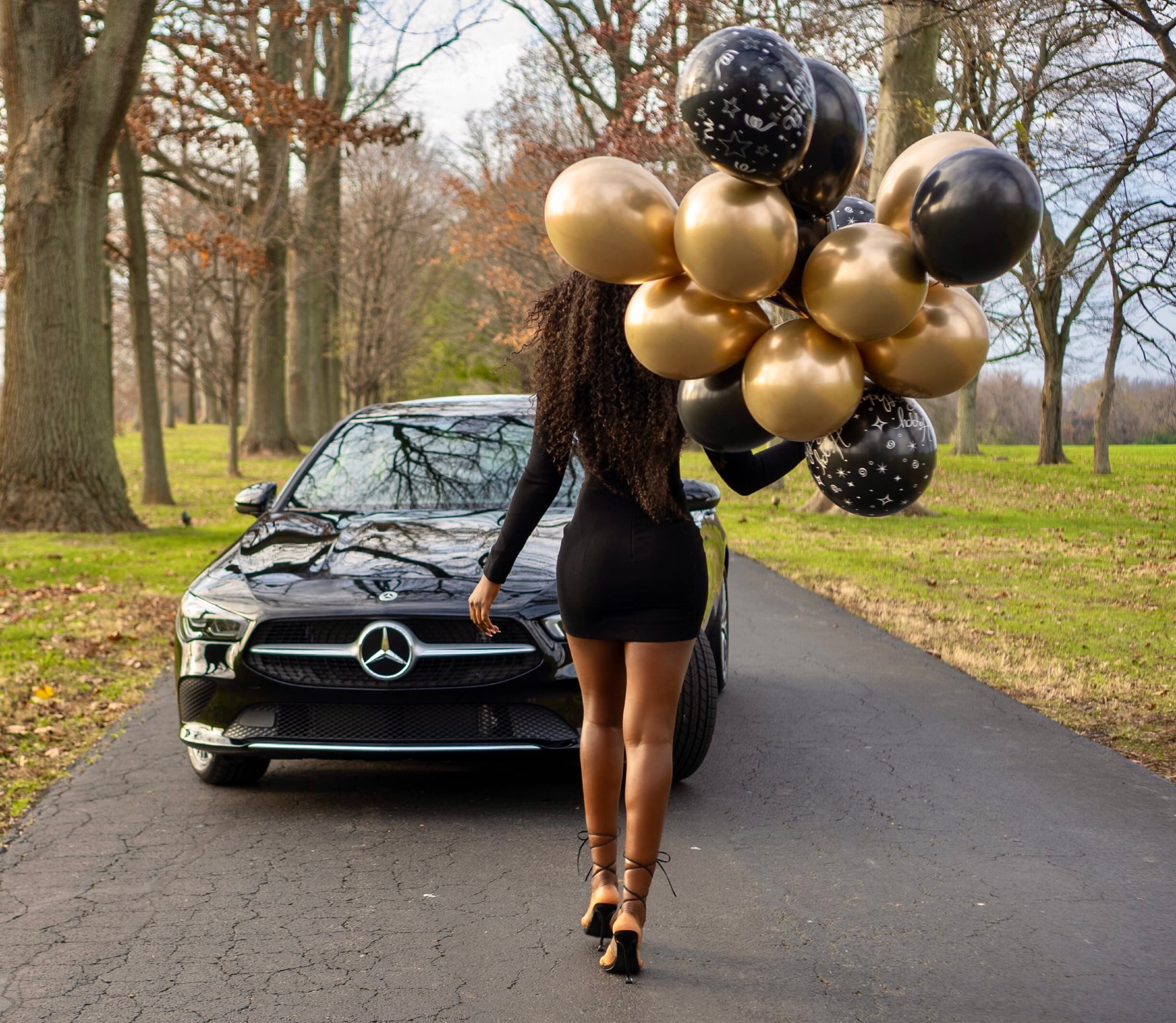 Lifestyle, woman with gold balloons beside black Mercedes in park