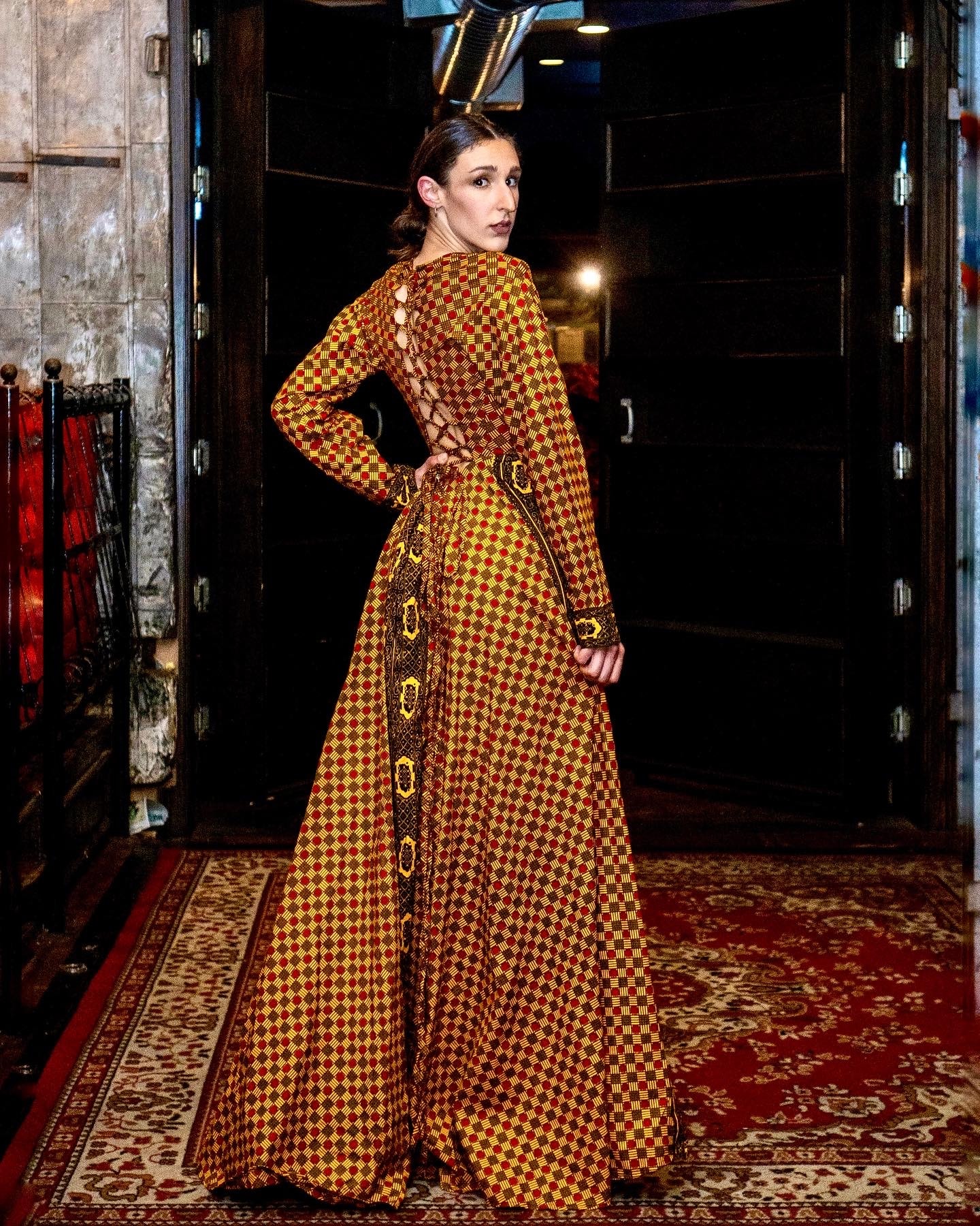Fashion editorial, woman in gold houndstooth gown at venue entrance